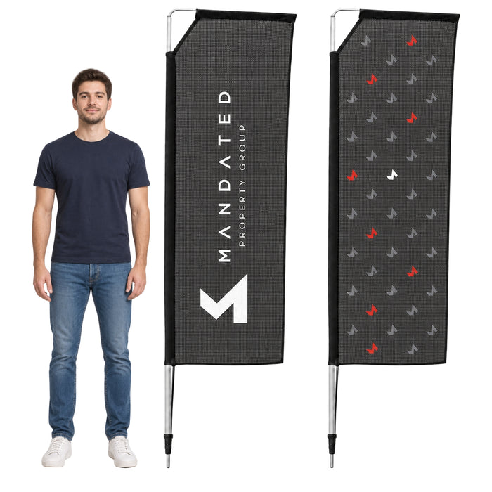 A man wearing a navy blue t-shirt and jeans stands next to two custom printed vertical flag banners on a white background. The left banner is dark gray with white text reading 'MANDATED PROPERTY GROUP' and a large white 'M' logo.