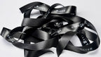 A pile of black satin ribbon with white 'LOTTER' branding printed repeatedly on it, photographed on a plain white background.