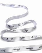 A white satin ribbon with a repeating black 'LOTTER PRINT CO.' logo pattern, coiled on a white background.