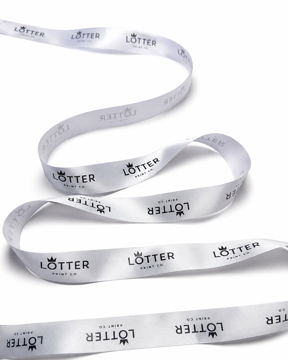 A white satin ribbon with a repeating black 'LOTTER PRINT CO.' logo pattern, coiled on a white background.